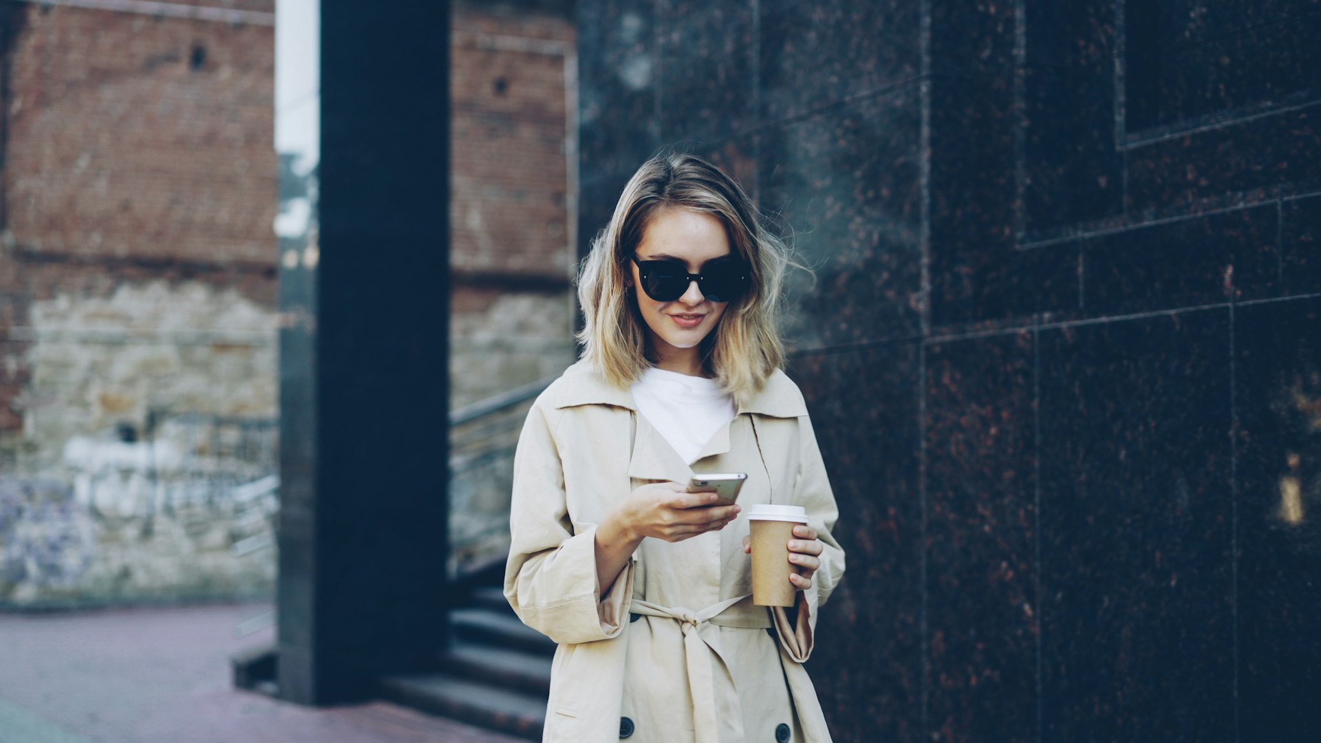 Woman with coffee and phone on city street
